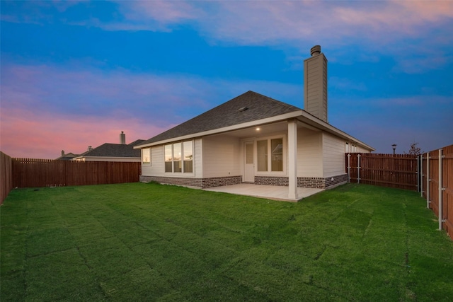 back house at dusk with a yard and a patio