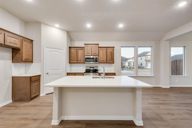 kitchen featuring stainless steel appliances, lofted ceiling, sink, and a center island with sink