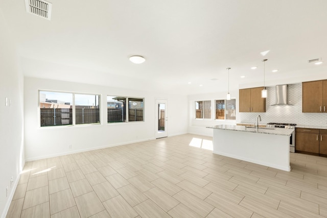 kitchen with sink, tasteful backsplash, stainless steel gas range oven, decorative light fixtures, and wall chimney exhaust hood