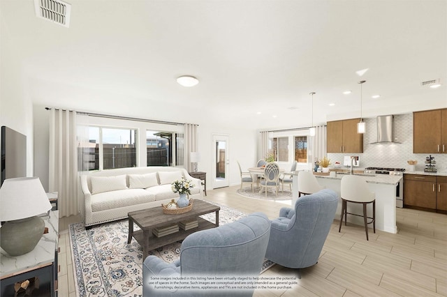 kitchen with sink, a center island with sink, hanging light fixtures, light stone countertops, and wall chimney range hood