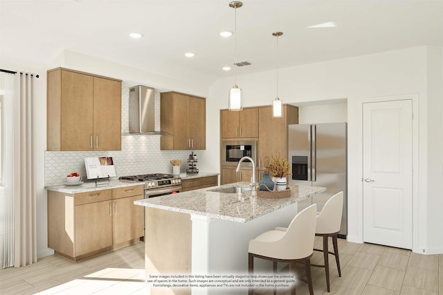 kitchen with decorative light fixtures, an island with sink, sink, stainless steel appliances, and wall chimney range hood