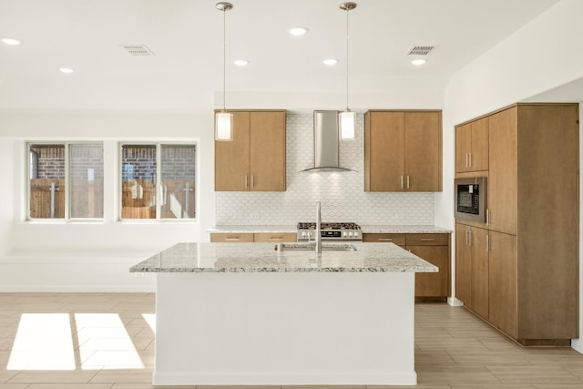 kitchen with appliances with stainless steel finishes, decorative light fixtures, decorative backsplash, wall chimney range hood, and a center island with sink