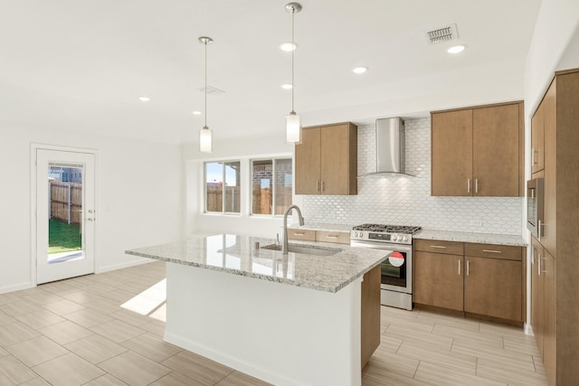 kitchen with decorative light fixtures, an island with sink, sink, gas stove, and wall chimney range hood