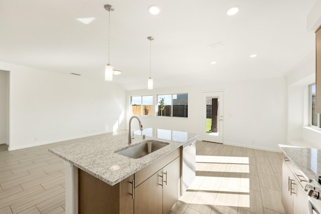 kitchen with pendant lighting, an island with sink, sink, stainless steel dishwasher, and light stone counters