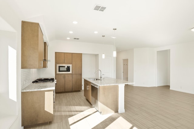 924 Alder Dr, Lavon, TX 75166 - kitchen featuring appliances with stainless steel finishes, brown cabinets, decorative backsplash, light stone counters, and an island with sink