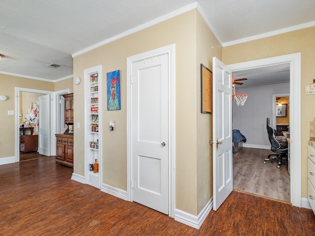 hallway with crown molding, built in shelves, and dark hardwood / wood-style floors