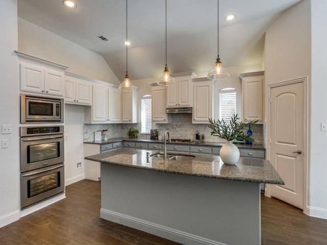 kitchen featuring vaulted ceiling, white cabinets, appliances with stainless steel finishes, dark stone countertops, and sink