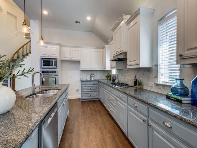 kitchen with dark stone countertops, appliances with stainless steel finishes, hanging light fixtures, sink, and lofted ceiling