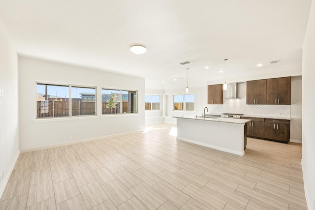 kitchen with sink, hanging light fixtures, backsplash, dark brown cabinets, and wall chimney exhaust hood