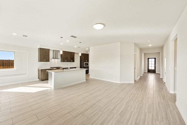 kitchen featuring pendant lighting, wall chimney range hood, sink, light stone countertops, and gas range