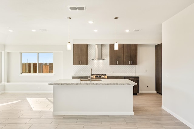 kitchen featuring pendant lighting, wall chimney range hood, tasteful backsplash, and light stone countertops