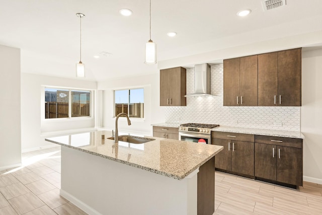 kitchen with sink, stainless steel gas stove, pendant lighting, light stone countertops, and wall chimney range hood