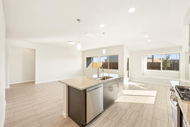 kitchen featuring sink, appliances with stainless steel finishes, an island with sink, pendant lighting, and light stone countertops