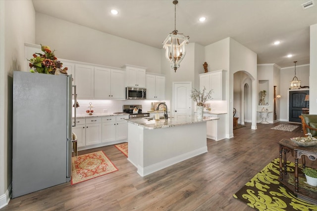 kitchen with decorative light fixtures, an island with sink, white cabinetry, light stone counters, and stainless steel appliances