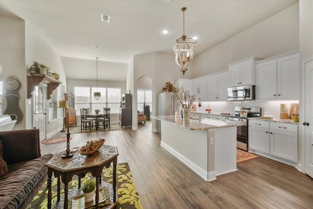 kitchen with appliances with stainless steel finishes, pendant lighting, white cabinets, and light stone counters