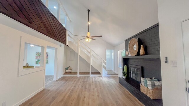 living room with high vaulted ceiling, ceiling fan, hardwood / wood-style floors, and a brick fireplace