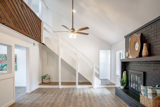 unfurnished living room with high vaulted ceiling, ceiling fan, a fireplace, and wood-type flooring