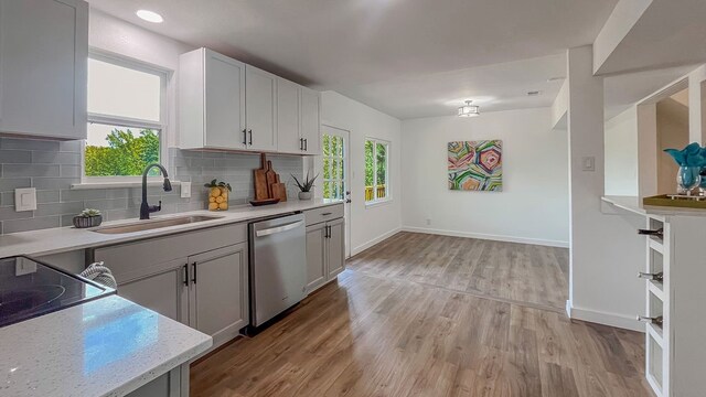 kitchen with light stone countertops, dishwasher, light hardwood / wood-style floors, sink, and decorative backsplash