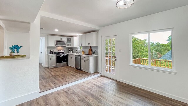 kitchen with light wood-type flooring, white cabinetry, tasteful backsplash, stainless steel appliances, and sink