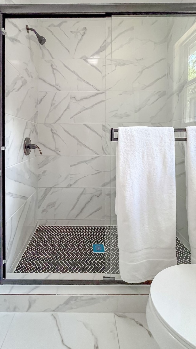 bathroom featuring a shower with door and toilet