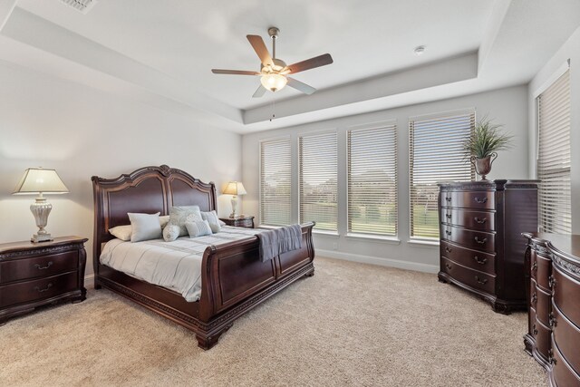 bedroom with light colored carpet, ceiling fan, and a tray ceiling