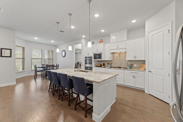 kitchen with stainless steel appliances, hardwood / wood-style floors, white cabinets, and a kitchen island with sink