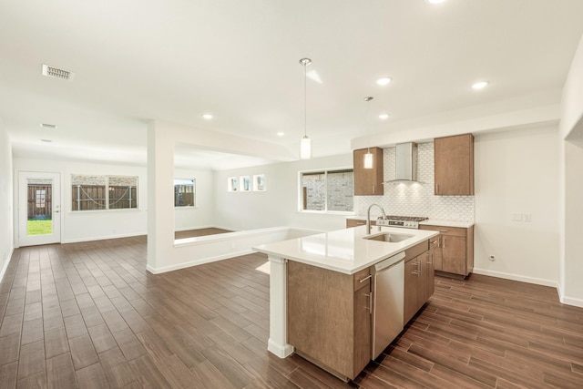 kitchen featuring sink, hanging light fixtures, a center island with sink, stainless steel dishwasher, and wall chimney range hood