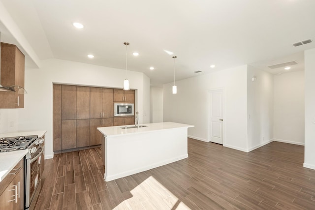 kitchen featuring built in microwave, sink, gas range, hanging light fixtures, and a kitchen island with sink