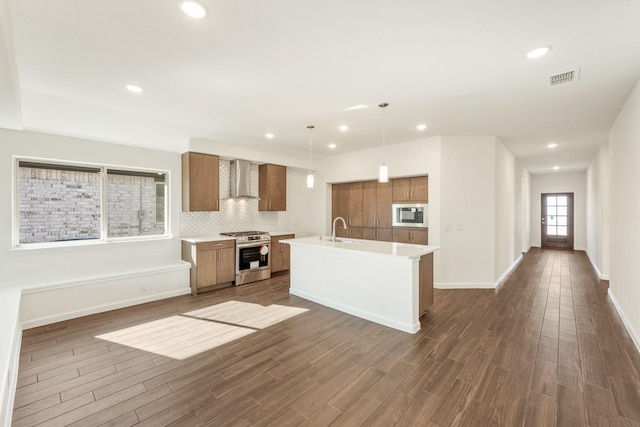 kitchen featuring sink, wall chimney range hood, hanging light fixtures, stainless steel appliances, and dark hardwood / wood-style floors