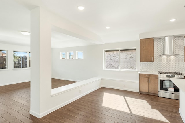 kitchen featuring wood-type flooring, stainless steel range with gas cooktop, a healthy amount of sunlight, decorative backsplash, and wall chimney range hood