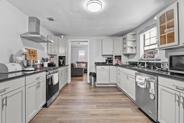 kitchen with stainless steel appliances, sink, white cabinetry, hardwood / wood-style flooring, and wall chimney range hood