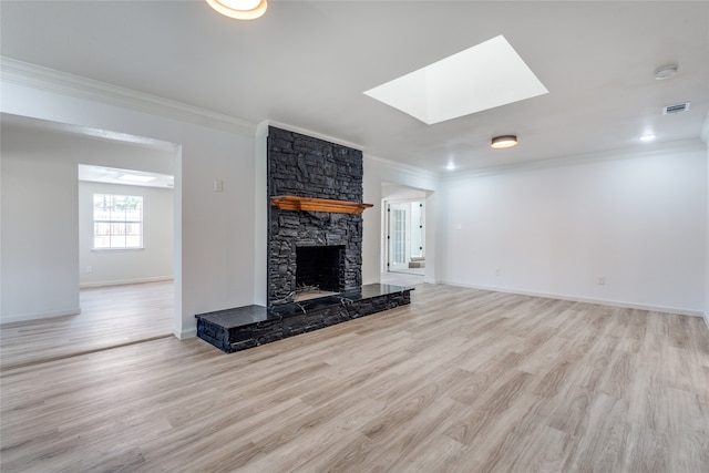 unfurnished living room with a skylight, a fireplace, ornamental molding, and light hardwood / wood-style flooring