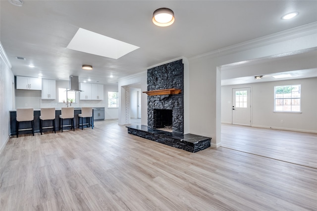 living room with light wood-type flooring, a skylight, a fireplace, and ornamental molding