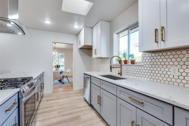 kitchen featuring light stone countertops, extractor fan, stainless steel appliances, sink, and a skylight