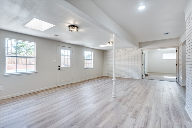 basement featuring light wood-type flooring, brick wall, and ceiling fan