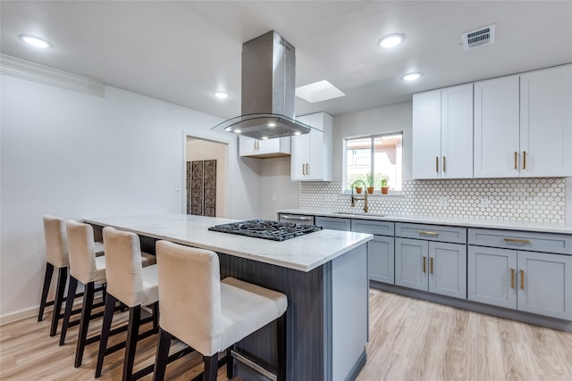 kitchen with light wood-type flooring, island range hood, stainless steel gas stovetop, and light stone counters