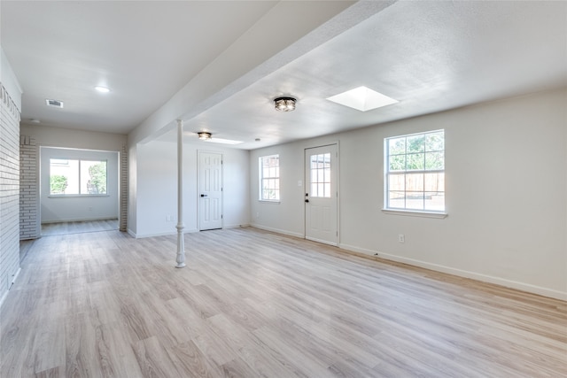 spare room with a skylight, light hardwood / wood-style floors, a textured ceiling, and a healthy amount of sunlight