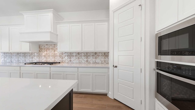 kitchen with premium range hood, stainless steel appliances, decorative backsplash, and white cabinets