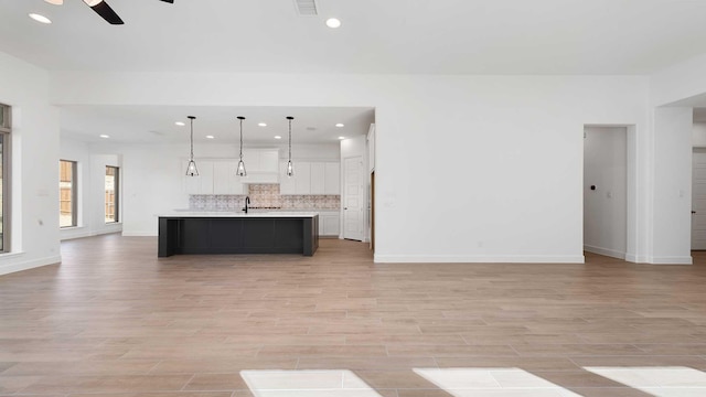 kitchen with sink, white cabinetry, decorative light fixtures, an island with sink, and backsplash