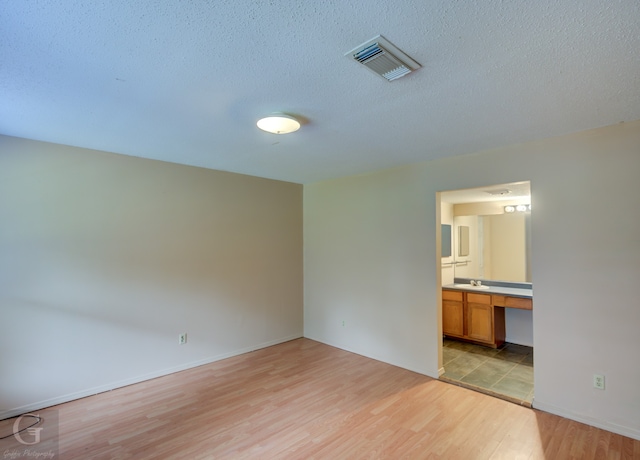 empty room with light wood-type flooring, built in desk, sink, and a textured ceiling