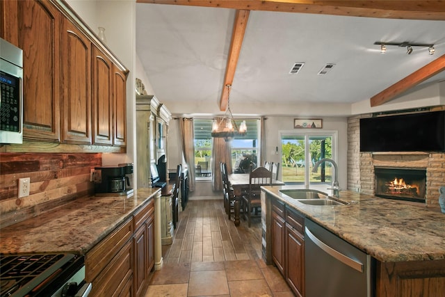 kitchen featuring stainless steel appliances, sink, a notable chandelier, a stone fireplace, and an island with sink