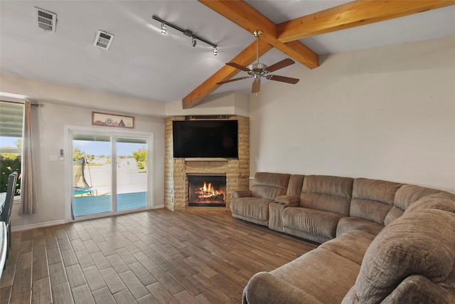 living room featuring vaulted ceiling with beams, ceiling fan, a stone fireplace, and rail lighting