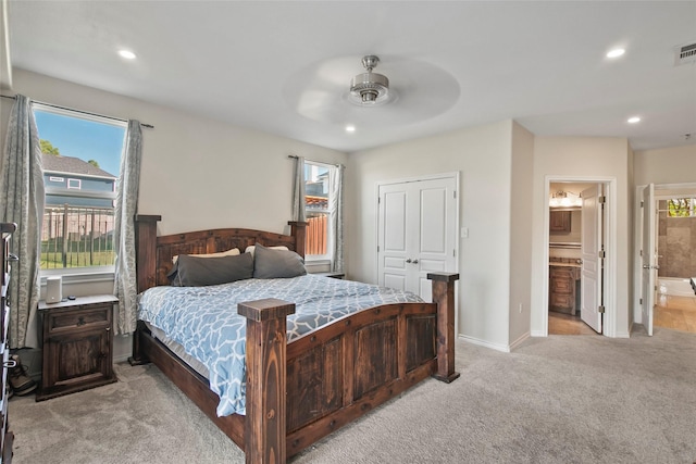 bedroom with multiple windows, ensuite bathroom, ceiling fan, and light colored carpet