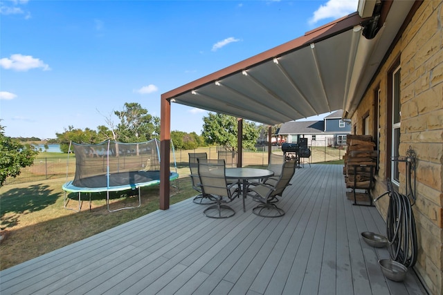 wooden deck with a trampoline, a lawn, and a water view