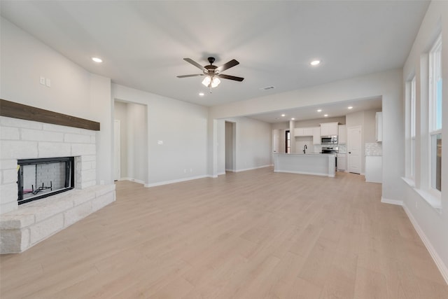 unfurnished living room with light hardwood / wood-style floors, a stone fireplace, ceiling fan, and sink