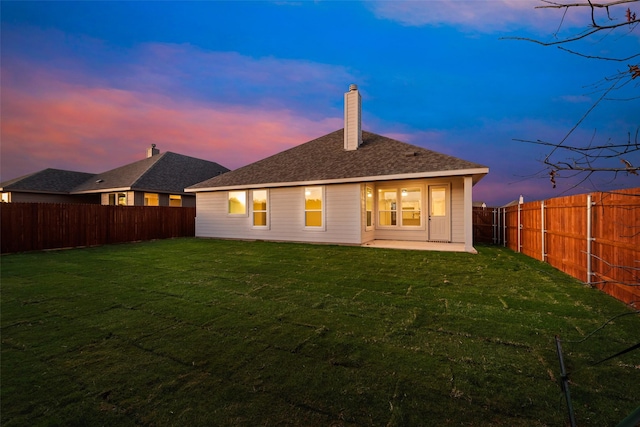 back house at dusk with a patio and a lawn