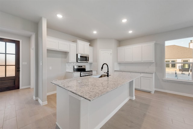 kitchen featuring a healthy amount of sunlight, white cabinetry, stainless steel appliances, and a kitchen island with sink