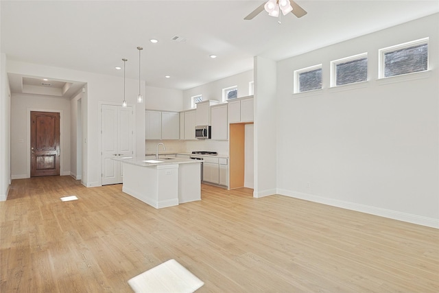 kitchen with pendant lighting, ceiling fan, light hardwood / wood-style floors, and a kitchen island with sink