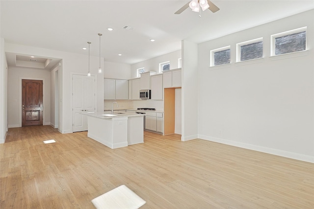 kitchen featuring stainless steel microwave, ceiling fan, light countertops, light wood finished floors, and an island with sink