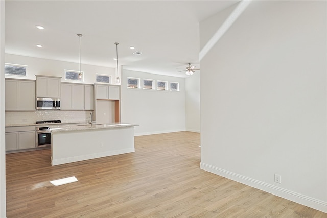 kitchen with appliances with stainless steel finishes, ceiling fan, backsplash, a sink, and a center island with sink